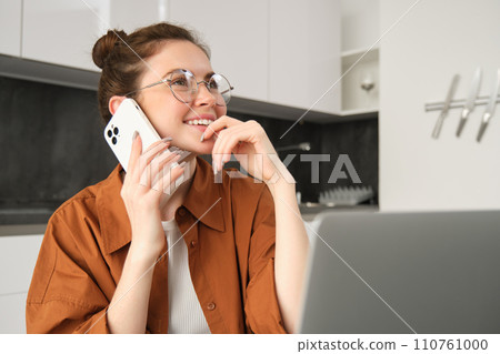 Portrait of woman working from home with laptop, making a phone call, using smartphone, looking thoughtful, order something online Portrait of woman working from home with laptop, making a phone call, using smartphone, looking thoughtful, order something online 110761000