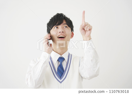 High school boy pointing upwards while calling on smartphone, white background 110763018