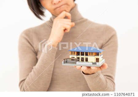 A middle-aged woman worries while holding a model of a detached house. 110764071