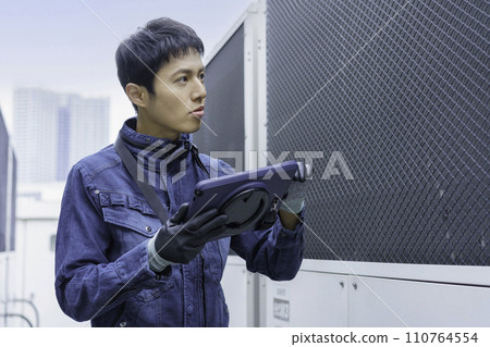 Portrait of a young man wearing denim work clothes doing inspection work on the roof of a building Photography cooperation: Ariake College of Education and Art 110764554