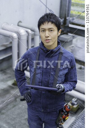 Portrait of a young man wearing denim work clothes doing inspection work on the roof of a building Photography cooperation: Ariake College of Education and Art 110764561