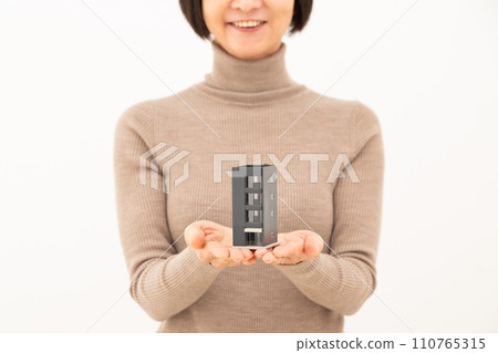 Middle-aged woman with a house model of a building Middle-aged woman with a house model of a building 110765315