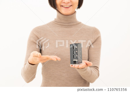 一位中年婦女微笑著拿著一棟建築物的房屋模型 一位中年婦女微笑著拿著一棟建築物的房屋模型 110765356