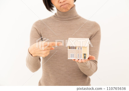 A middle-aged woman worries while holding a model of a detached house. A middle-aged woman worries while holding a model of a detached house. 110765636