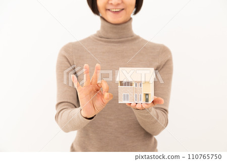 一位中年婦女拿著獨立屋的模型,做一個圓圈標誌 一位中年婦女拿著獨立屋的模型,做一個圓圈標誌 110765750