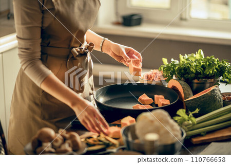 Hands of young woman put pumpkin on frying pan for baking in the kitchen. The concept of healthy eating Hands of young woman put pumpkin on frying pan for baking in the kitchen. The concept of healthy eating 110766658