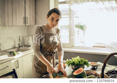 Young woman cuts a pumpkin for baking in an apron in the kitchen. looks at camera. The concept of healthy nutrition 110766659