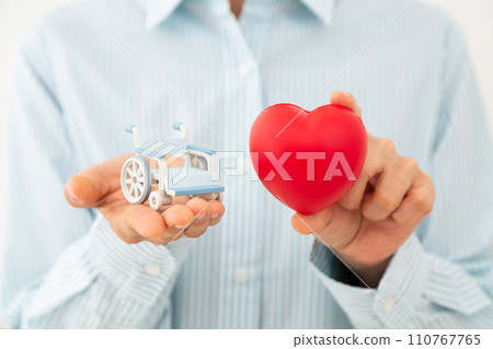Hands of a middle-aged woman holding a heart and a model of a wheelchair 110767765