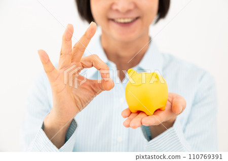 A middle-aged woman holding a pig piggy bank and making a circle sign A middle-aged woman holding a pig piggy bank and making a circle sign 110769391