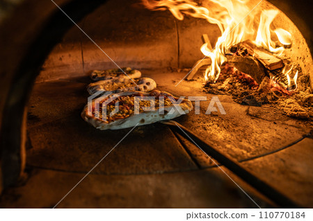Traditional oven for baking pizza with burning wood and shovel. The cook rotates the pizza in the oven to ensure even baking Traditional oven for baking pizza with burning wood and shovel. The cook rotates the pizza in the oven to ensure even baking 110770184
