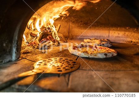 Traditional oven for baking pizza with burning wood and shovel. The cook rotates the pizza in the oven to ensure even baking Traditional oven for baking pizza with burning wood and shovel. The cook rotates the pizza in the oven to ensure even baking 110770185