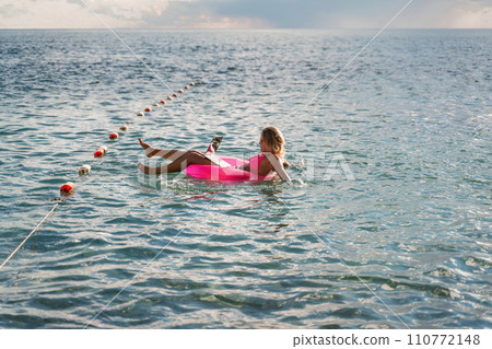 Woman works on laptop in sea. Freelancer, blond woman in sunglases floating on an inflatable big pink donut with a laptop in the sea at sunset. People summer vacation rest lifestyle concept. 110772148