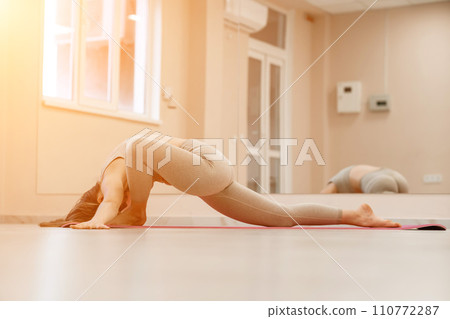 Girl does yoga. Young woman practices asanas on a beige one-ton background. 110772287