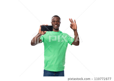 young charismatic american man in green t-shirt and jeans showing smartphone screen with mockup 110772877