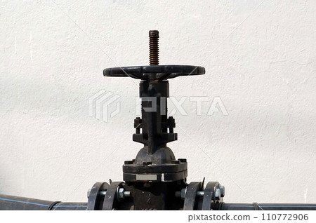 Close up of the big black valve on the pipeline with white wall background Close up of the big black valve on the pipeline with white wall background 110772906