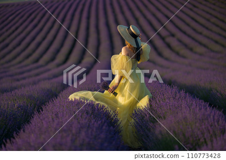 Back view woman lavender sunset. Happy woman in yellow dress holds lavender bouquet. Aromatherapy concept, lavender oil, photo session in lavender 110773428