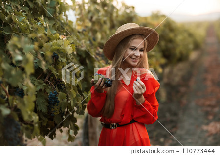 portrait of a happy woman in the summer vineyards at sunset. woman in a hat and smiling. portrait of a happy woman in the summer vineyards at sunset. woman in a hat and smiling. 110773444