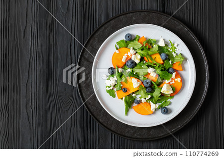 arugula persimmon cheese berries salad, top view arugula persimmon cheese berries salad, top view 110774269