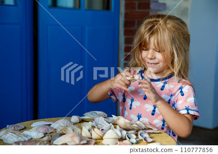 Little preschool girl with variation of different shells and clams at home. Happy child with collected shell from Normandy, France. Children, education, vacation concept. Little preschool girl with variation of different shells and clams at home. Happy child with collected shell from Normandy, France. Children, education, vacation concept. 110777856