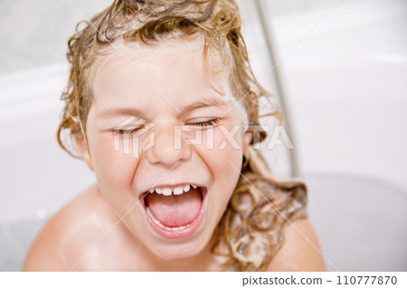 Cute child with shampoo foam and bubbles on hair taking bath. Portrait of happy smiling preschool girl health care and hygiene concept. Washes hair by herself. Cute child with shampoo foam and bubbles on hair taking bath. Portrait of happy smiling preschool girl health care and hygiene concept. Washes hair by herself. 110777870