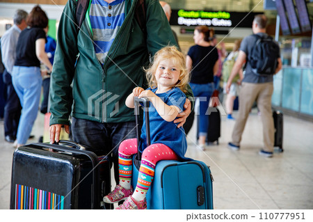 Cute little toddler girl and father at the airport. Happy family traveling by plane, making vacations. Young dad and baby daughter with suitcases waiting for flight. Family going on journey. Ireland Cute little toddler girl and father at the airport. Happy family traveling by plane, making vacations. Young dad and baby daughter with suitcases waiting for flight. Family going on journey. Ireland 110777951