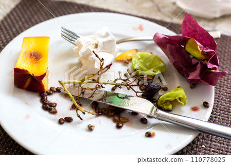 Fruit cores, leftover food and dirty napkins in a plate on the table 110778025