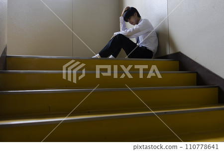 A worried male student sitting on the stairs A worried male student sitting on the stairs 110778641