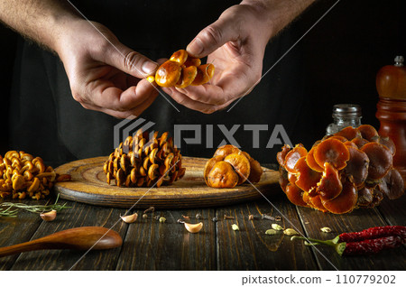 A chef cleans fresh raw mushrooms with his hands in a restaurant kitchen. Concept of preparing dietary Flammulina velutipes for lunch A chef cleans fresh raw mushrooms with his hands in a restaurant kitchen. Concept of preparing dietary Flammulina velutipes for lunch 110779202