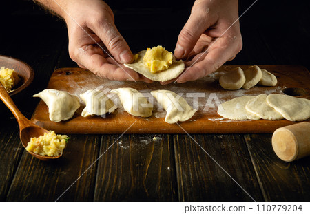 Modeling dumplings by the hands of a chef. The concept of preparing dumplings on the kitchen table from dough and boiled potatoes for a delicious breakfast 110779204