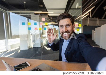 Businessman inside office taking selfie, scared mature man looking into smartphone camera, waving hand greeting, using video call app, chatting talking joyfully with friends. 110779828