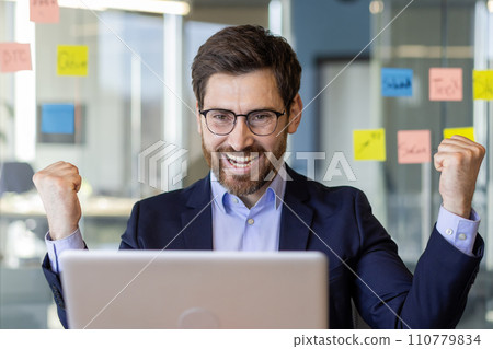 Businessman winner close up inside office, joyful man celebrating victory and successful achievement results mature experienced boss holding hands up, received notification on laptop. Businessman winner close up inside office, joyful man celebrating victory and successful achievement results mature experienced boss holding hands up, received notification on laptop. 110779834