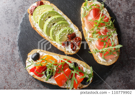 Set of open toasted bruschetta with arugula, jamon, vegetables, cream cheese close-up on a slate board. Horizontal top view 110779902