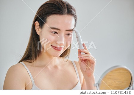 A woman in her 30s shaving her face with an electric shaver A woman in her 30s shaving her face with an electric shaver 110781428