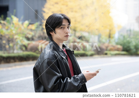 冬天的西新宿,一個穿著皮夾克、拿著智慧型手機的年輕人 冬天的西新宿,一個穿著皮夾克、拿著智慧型手機的年輕人 110781621