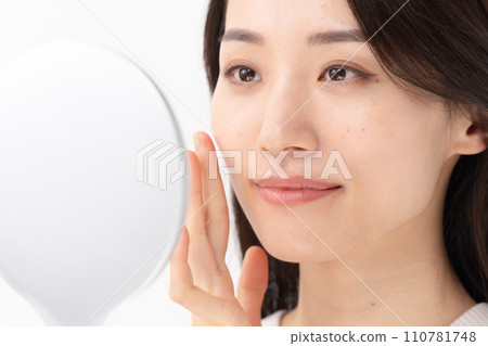 A woman checking her skin with a hand mirror 110781748