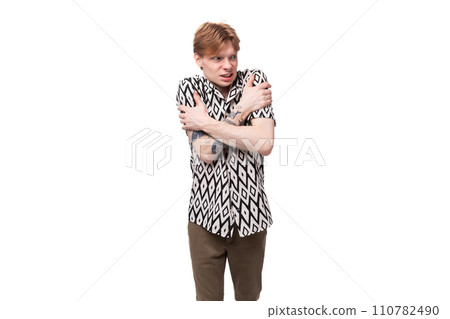 a young European man with golden hair is dressed in a stylish shirt with a pattern crossed his arms a young European man with golden hair is dressed in a stylish shirt with a pattern crossed his arms 110782490