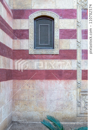 Mamluk architecture: rustic charm, weathered wooden window with star pattern, against aged brick wall 110782574