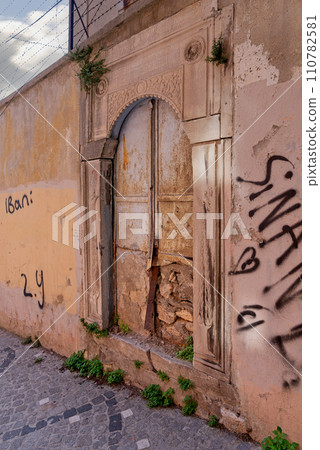Grungy abandoned entrance with rusted metal door, in a cobblestone narrow street Grungy abandoned entrance with rusted metal door, in a cobblestone narrow street 110782581