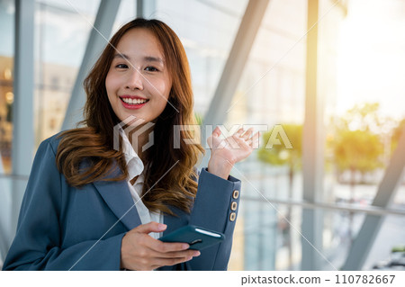 Smiling young woman using her smartphone for messaging, browsing and calling on a bright and modern urban background. 110782667