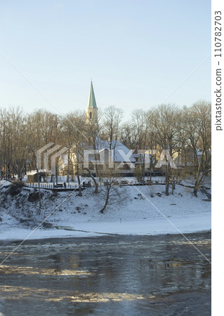 Winter city landscapes of Kuldiga, Latvia. Ancient buildings through a pattern of trees. Vertical frame. he Evangelical Lutheran Church of Saint Catherine. View from across the Venta Rive. High 110782703