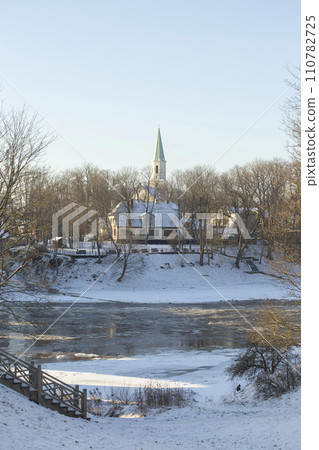 Winter city landscapes of Kuldiga, Latvia. Ancient buildings through a pattern of trees. Vertical frame. he Evangelical Lutheran Church of Saint Catherine. View from across the Venta Rive. High 110782725