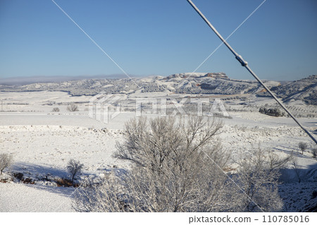Snow. Winter landscape covered in a white blanket of snow covering mountains and roads. Trees with snow. Clear day. White blanket due to a storm with heavy snowfall. In Spain. January. 2024. 110785016