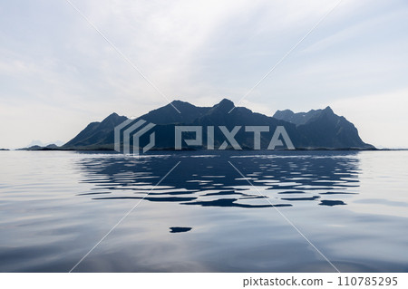 Glassy waters reflect Lofoten's jagged peaks in a serene, diffused light 110785295