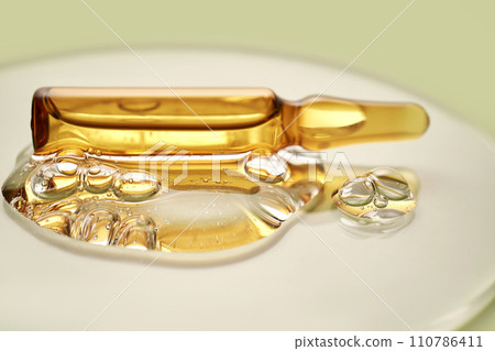 Ampoule in a drop of cosmetic gel on a green background. Ampoule in a drop of cosmetic gel on a green background. 110786411