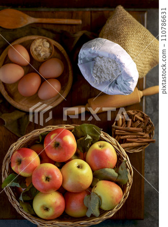Apples and cinnamon, flour and eggs are used in baking. Ingredients for making homemade apple pie on dark rustic background, top view. Classic autumn dessert Apples and cinnamon, flour and eggs are used in baking. Ingredients for making homemade apple pie on dark rustic background, top view. Classic autumn dessert 110786631