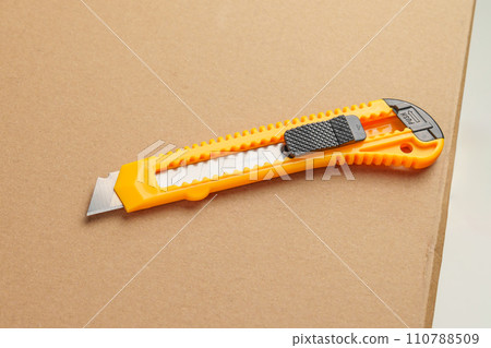 Box cutter on a parcel cardboard box close up. Retractable utility knife Box cutter on a parcel cardboard box close up. Retractable utility knife 110788509