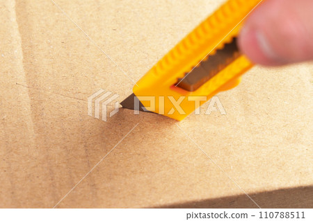 Unboxing parcel box. Opening cardboard package with utility knife. Cutting brown kraft paper close up Unboxing parcel box. Opening cardboard package with utility knife. Cutting brown kraft paper close up 110788511
