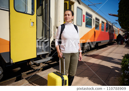 Full length female tourist holding suitcase, standing on the train station platform against colorful train background 110788909