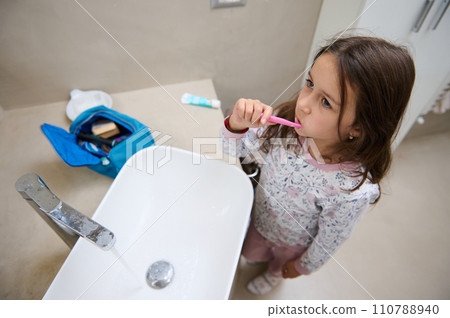 View from above of a child girl brushing teeth, standing at white washbasin in the home bathroom. Dental hygiene concept View from above of a child girl brushing teeth, standing at white washbasin in the home bathroom. Dental hygiene concept 110788940
