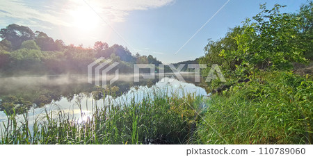 river is covered with fog at dawn. Forest is reflected in the river in summer river is covered with fog at dawn. Forest is reflected in the river in summer 110789060